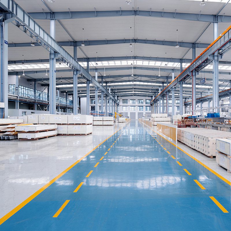 Wide-angle interior view of Reyeah's modern manufacturing facility, showcasing a clean production floor with blue epoxy coating, high-bay structure, and organized stacked materials